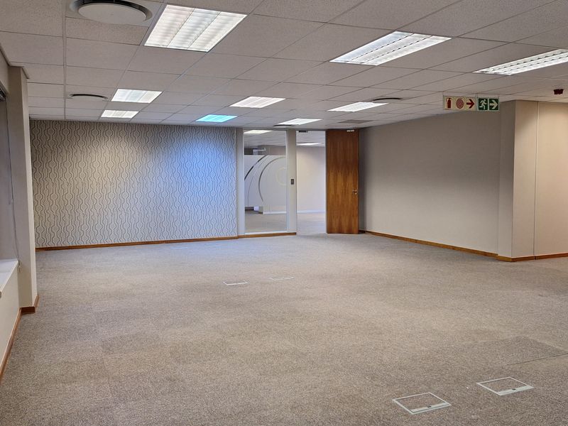 Spacious, open-plan office area featuring carpeted flooring, recessed ceiling lighting, and a decorative accent wall, providing a versatile workspace.