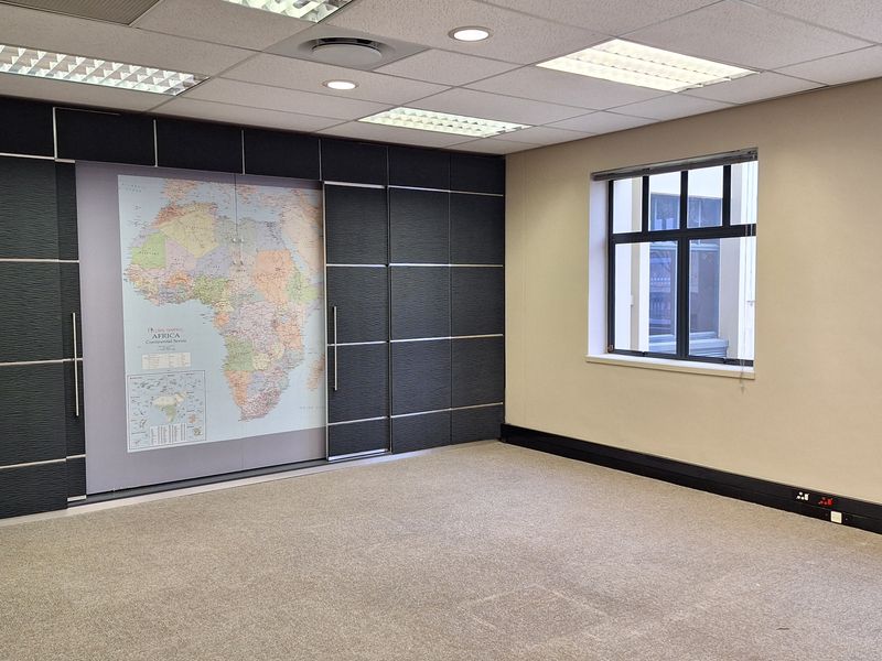 A professional office space featuring a suspended acoustic ceiling, recessed lighting, carpeted flooring, and a built-in feature wall with integrated cabinetry.