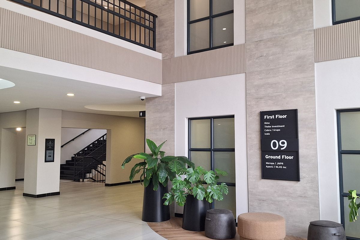 Modern double-volume office building lobby featuring tiled flooring, a mezzanine level with black metal railings, and integrated tenant directory signage.