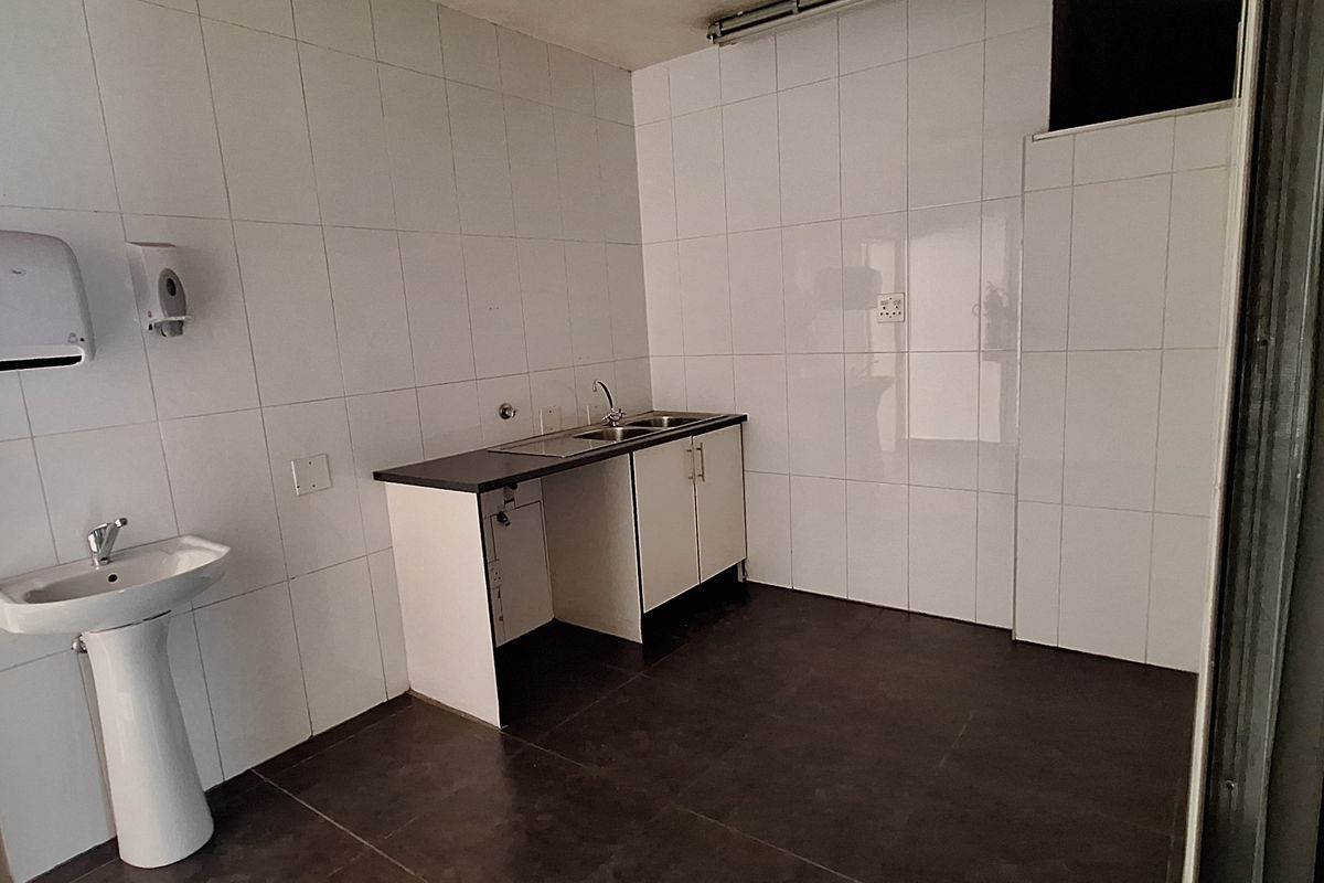 A functional office kitchenette featuring tiled walls, a pedestal basin, and a compact base cabinet with a sink.