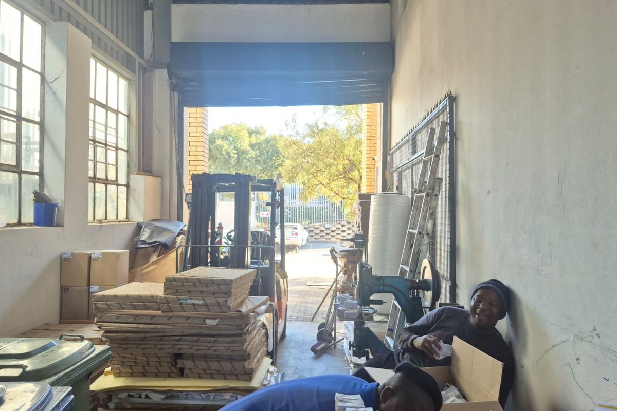 Industrial warehouse or garage space featuring high ceilings, large steel-framed windows, and a wide roller shutter door providing access to the exterior.