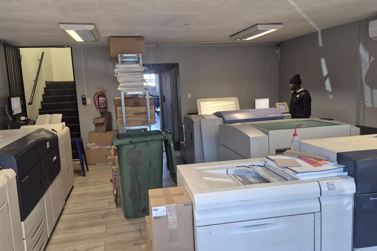 Industrial utility space featuring tiled flooring, wall-mounted air conditioning, and fluorescent lighting, currently utilized as a printing and production area.