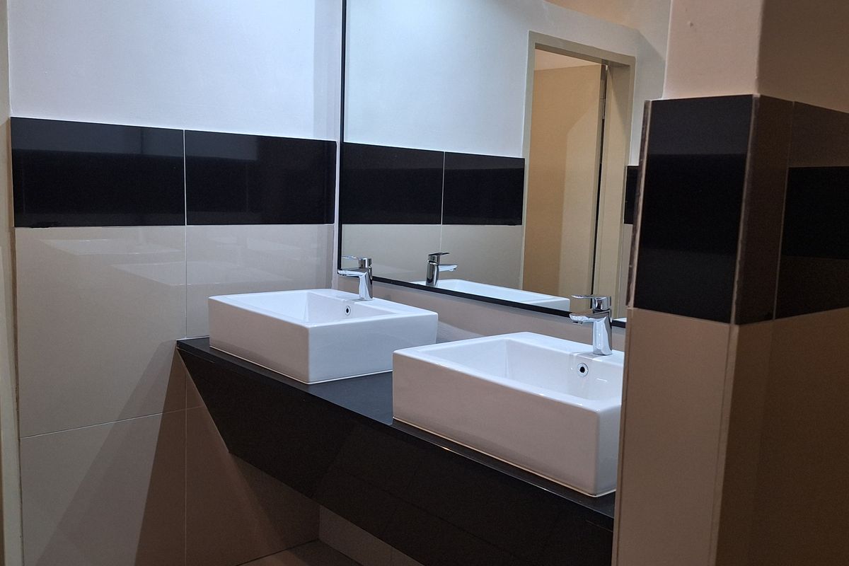 Modern office bathroom featuring a floating vanity with dual vessel sinks, chrome faucets, and a large wall-mounted mirror with contrasting black and beige tiling.