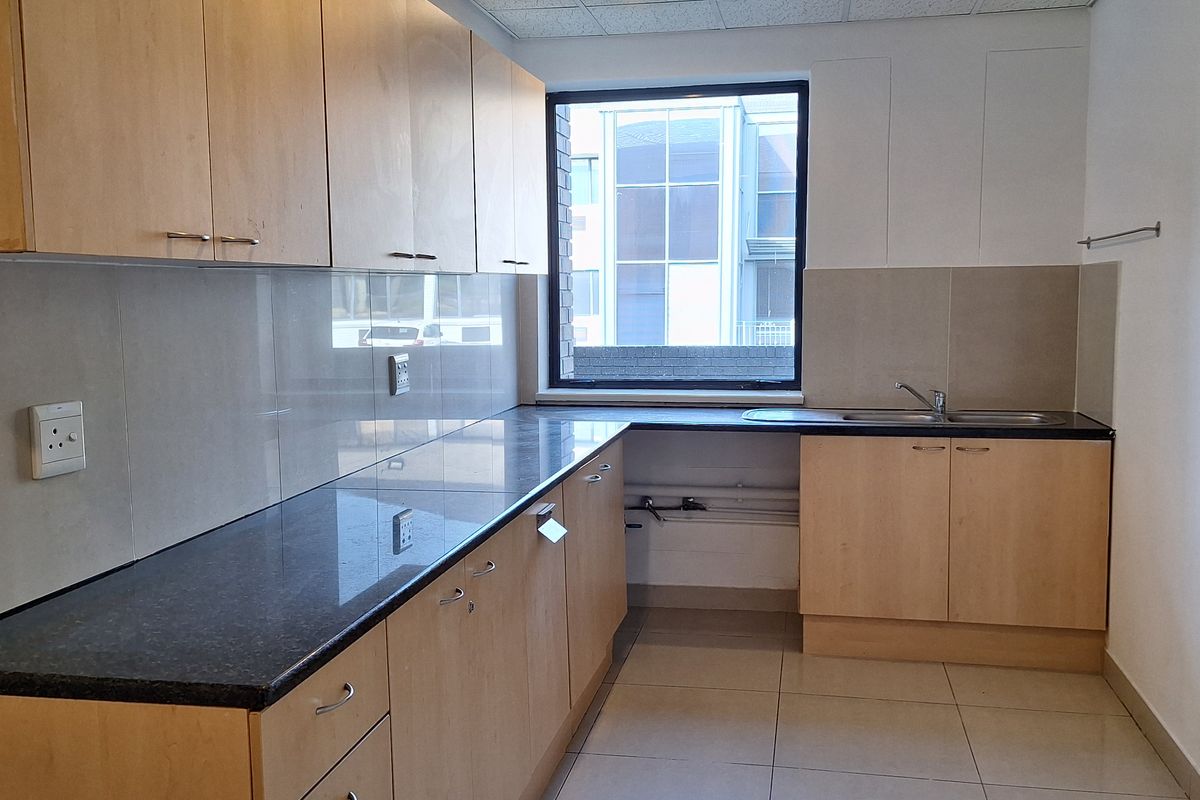 A functional office kitchenette featuring light wood cabinetry, dark granite countertops, a stainless steel sink, and tiled flooring.