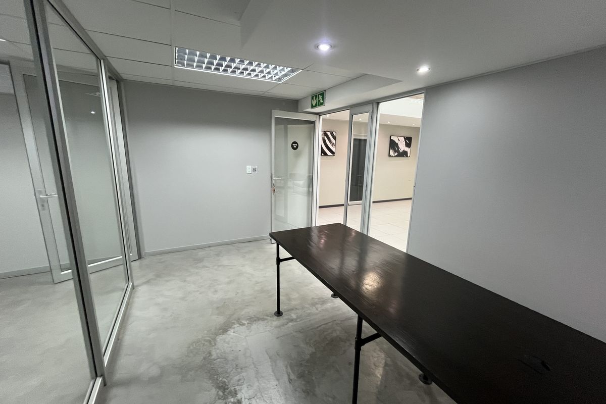A minimalist office space featuring polished concrete floors, glass partition walls, and recessed lighting, offering a clean and professional environment.