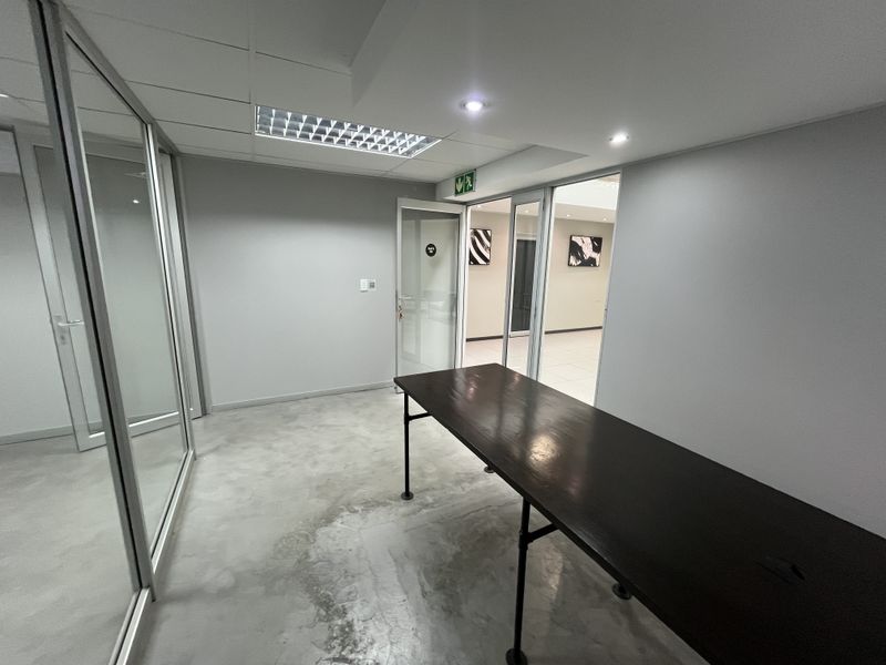 A minimalist office space featuring polished concrete floors, glass partition walls, and recessed lighting, offering a clean and professional environment.