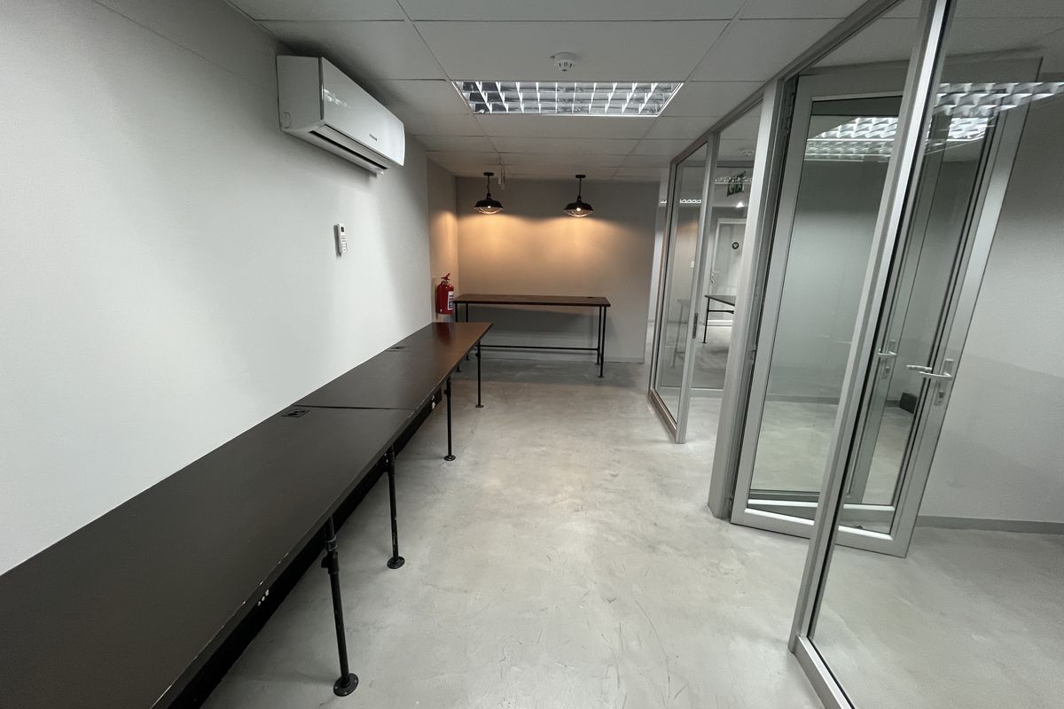 A modern, minimalist office space featuring glass partitions, suspended ceilings, recessed lighting, and an integrated air conditioning unit.