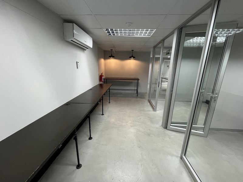 A modern, minimalist office space featuring glass partitions, suspended ceilings, recessed lighting, and an integrated air conditioning unit.
