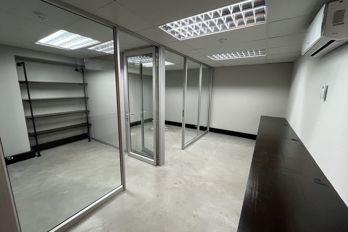 Modern office space featuring glass partitions, polished concrete floors, recessed lighting, and a split-system air conditioner, offering a clean and professional work environment.