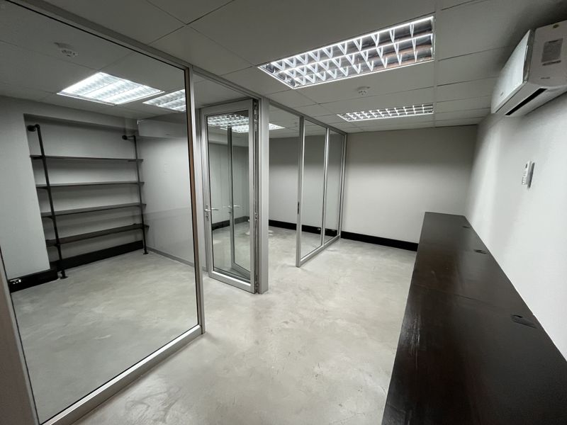 Modern office space featuring glass partitions, polished concrete floors, recessed lighting, and a split-system air conditioner, offering a clean and professional work environment.