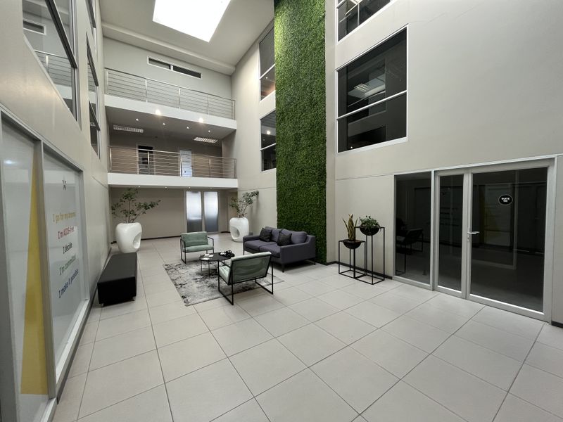 Modern office atrium featuring a double-volume space, skylight, vertical garden wall, and mezzanine levels with glass partitions and stainless steel balustrades.