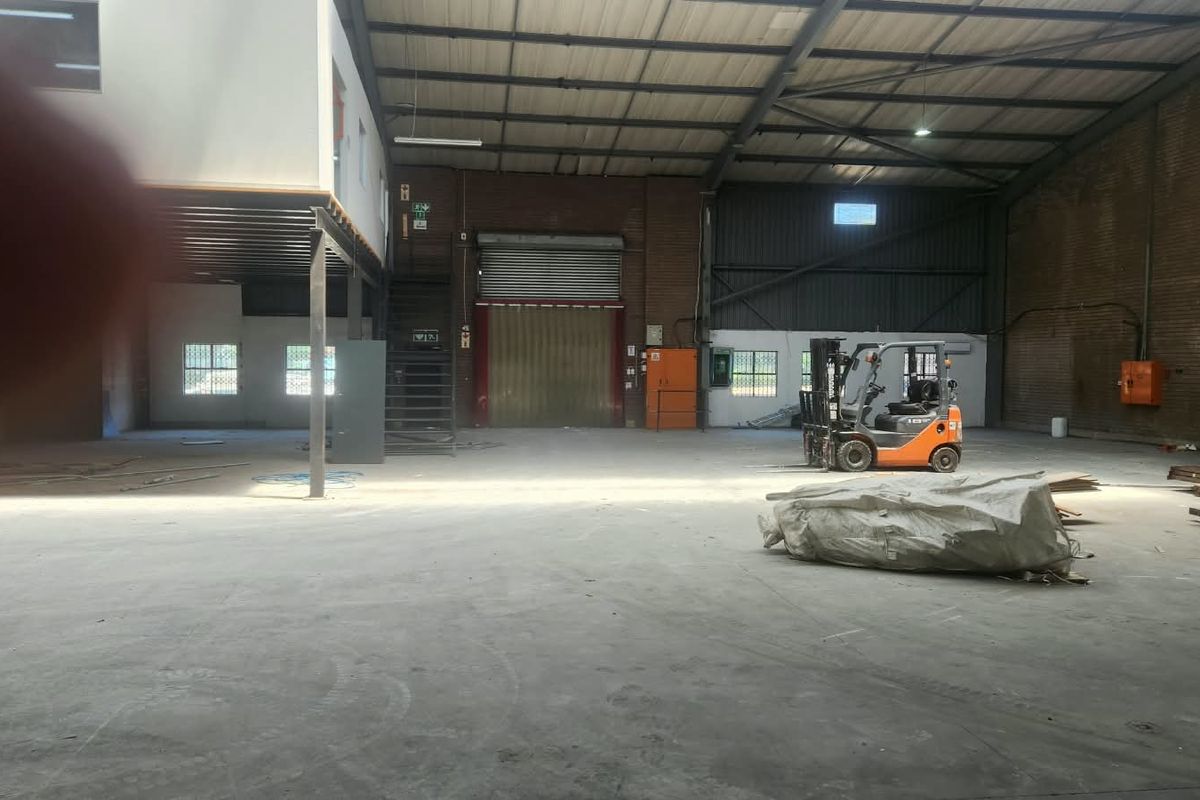 Spacious industrial warehouse featuring high ceilings with exposed steel trusses, a mezzanine level, concrete flooring, and a large roller shutter door for access.