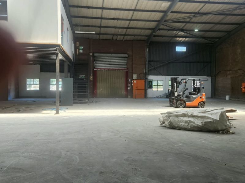 Spacious industrial warehouse featuring high ceilings with exposed steel trusses, a mezzanine level, concrete flooring, and a large roller shutter door for access.