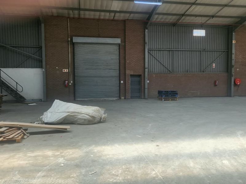 Spacious industrial warehouse unit featuring high ceilings, exposed brick walls, a large roller shutter door, and a steel staircase for mezzanine access.