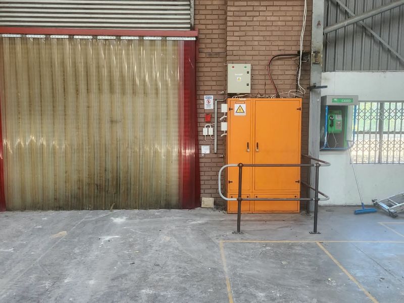 Industrial utility space featuring a large roller shutter door with PVC strip curtains, exposed brick walls, and fixed electrical infrastructure.