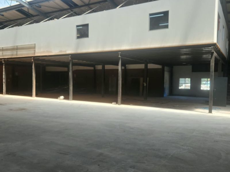 Spacious industrial open-plan warehouse area featuring a steel mezzanine level, exposed roof trusses, and concrete flooring, suitable for various commercial or industrial uses.