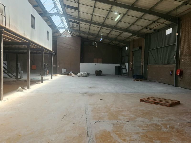 Spacious industrial warehouse featuring high ceilings with skylights, exposed brickwork, concrete flooring, and a mezzanine level, suitable for various commercial or storage operations.