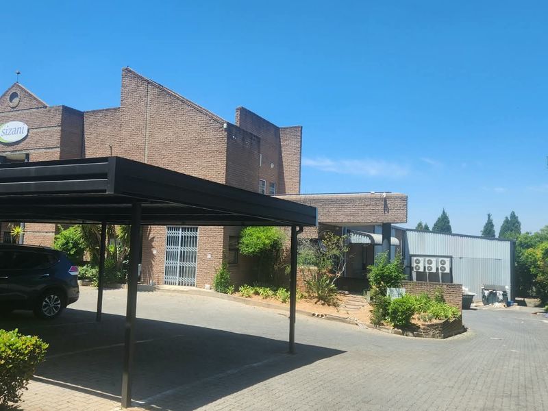 Front exterior view of the industrial property featuring a brick facade, paved driveway, and a covered carport area.