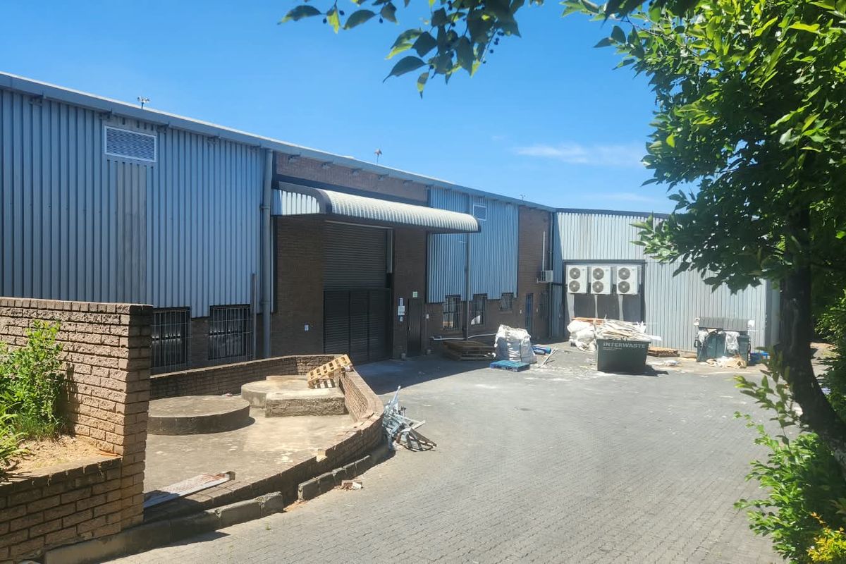 Rear exterior view of an industrial property featuring corrugated metal cladding, brickwork, a roller shutter door, and a paved yard area.