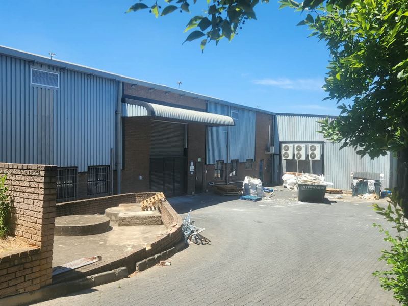 Rear exterior view of an industrial property featuring corrugated metal cladding, brickwork, a roller shutter door, and a paved yard area.