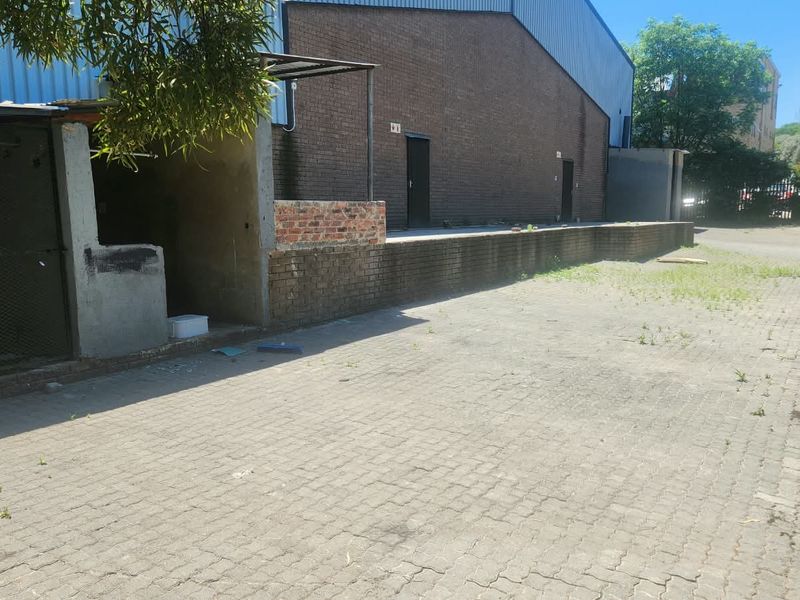 Rear industrial yard featuring a brick loading dock, paved surface, and metal-clad warehouse exterior.