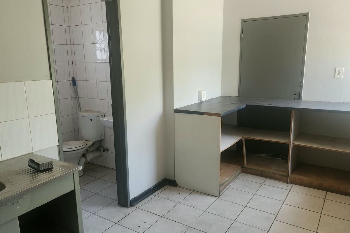 A basic industrial kitchen area featuring built-in cabinetry, a stainless steel sink, and tiled flooring, with an adjacent small bathroom.