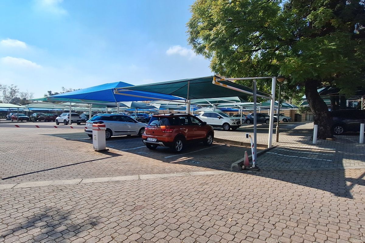 A paved outdoor parking area featuring multiple shaded parking bays with overhead shade cloth structures.