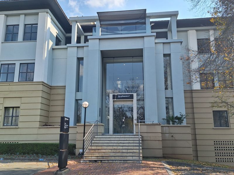 Front elevation of a modern office building featuring a prominent glass entrance, concrete staircase, and professional signage.