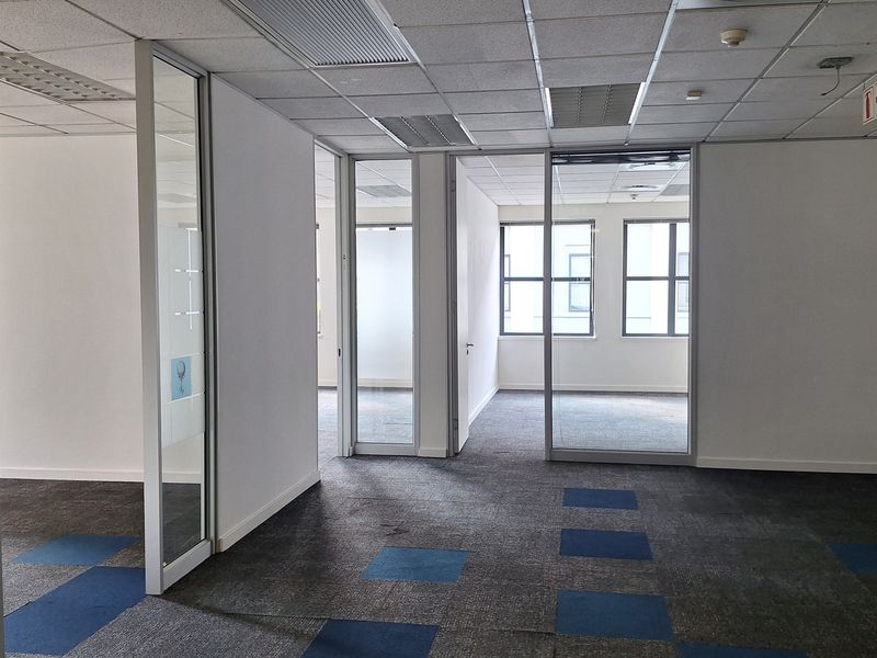 An empty office space featuring glass partitions, suspended ceilings with recessed lighting, and patterned carpet tiles, offering a clean and professional layout.