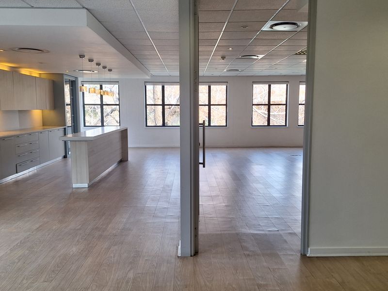 Spacious open-plan office area featuring modern laminate flooring, a built-in kitchenette with island, and large windows providing ample natural light.