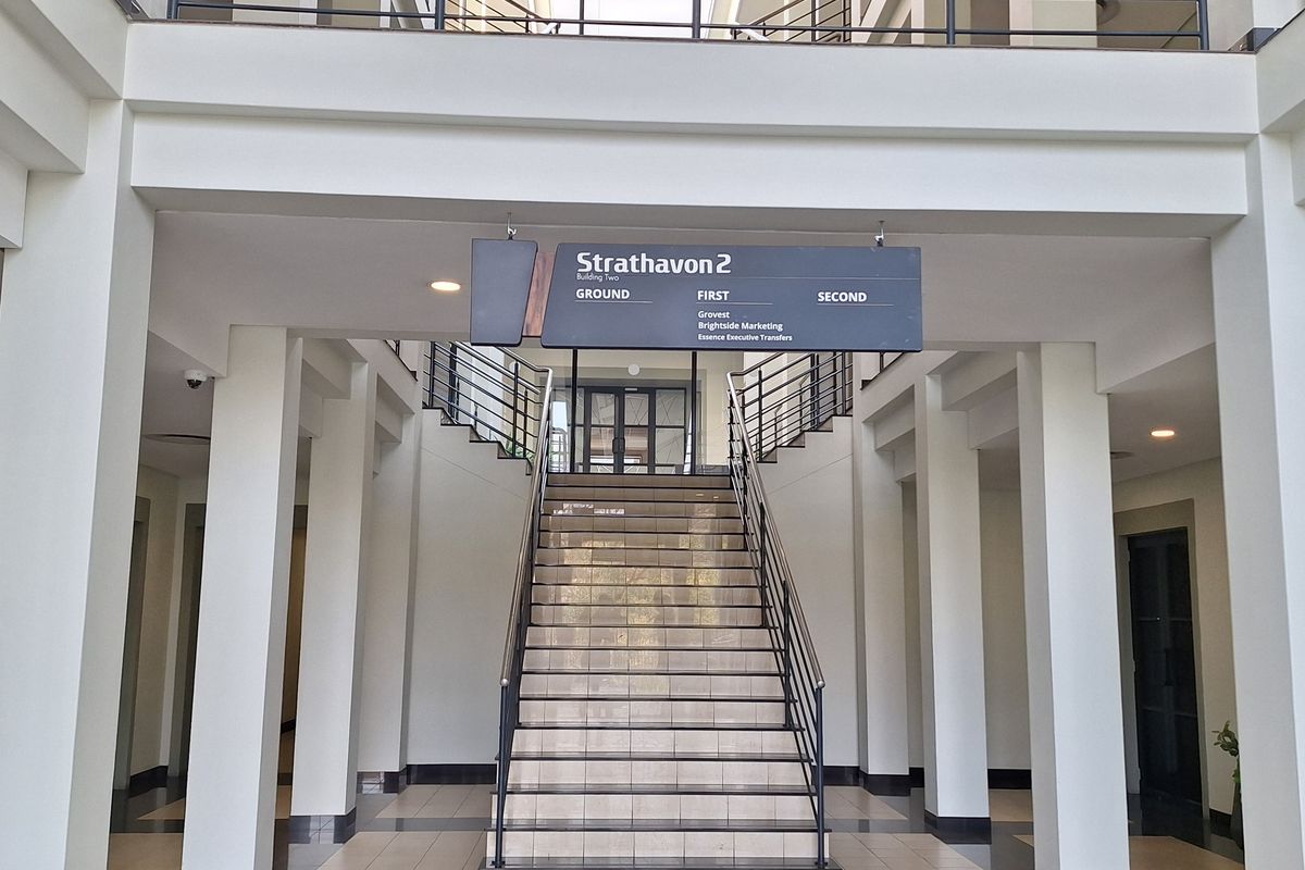 Spacious office building entrance lobby featuring a central staircase, tiled flooring, and clear directory signage for multiple office levels.