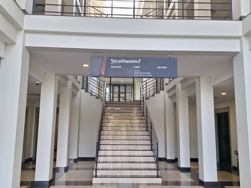 Spacious office building entrance lobby featuring a central staircase, tiled flooring, and clear directory signage for multiple office levels.