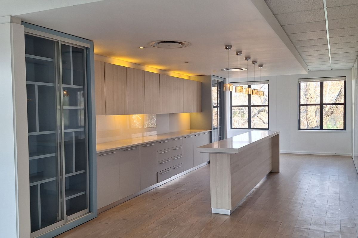 Modern office kitchen area featuring sleek built-in cabinetry, stone countertops, a central island, and integrated under-cabinet lighting in a bright, open-plan space.