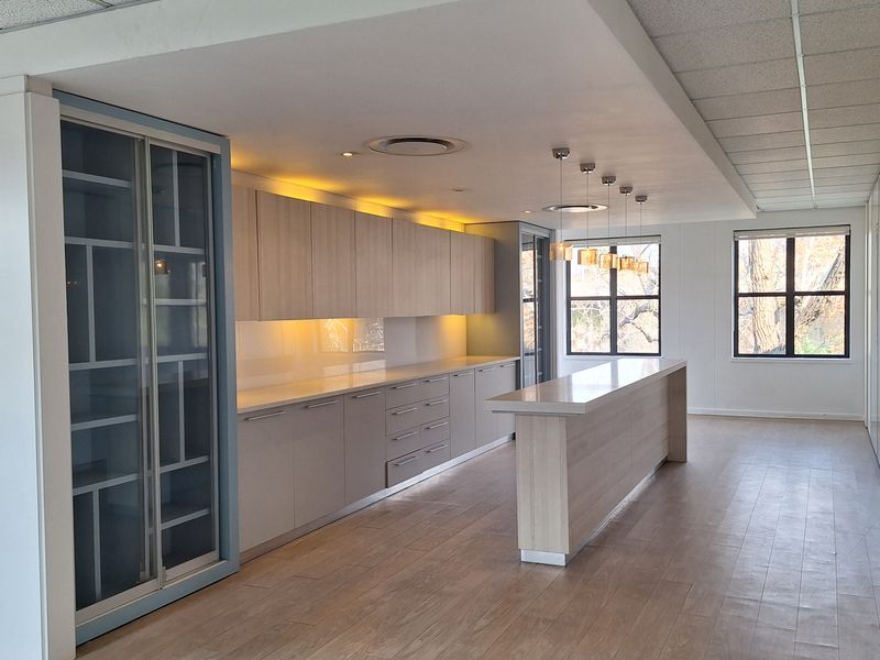 Modern office kitchen area featuring sleek built-in cabinetry, stone countertops, a central island, and integrated under-cabinet lighting in a bright, open-plan space.