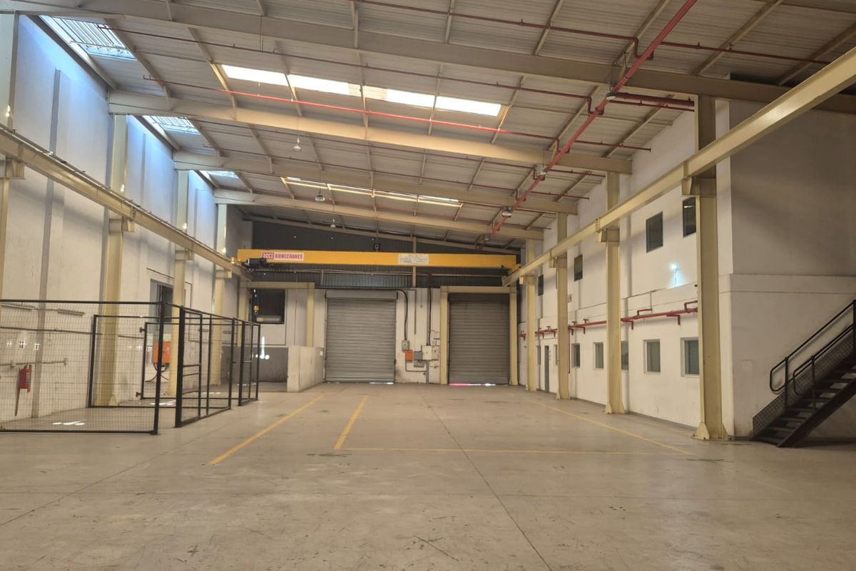 Spacious industrial warehouse featuring high ceilings, overhead crane, roller shutter doors, and concrete flooring, suitable for manufacturing or logistics operations.