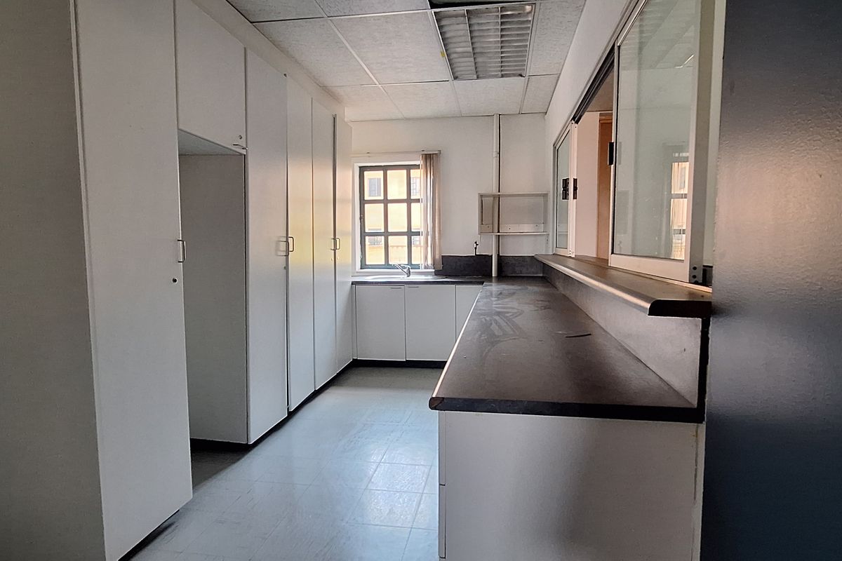 A functional office kitchenette featuring built-in white cabinetry, a dark laminate countertop, and a small sink, providing essential utility space for the workplace.