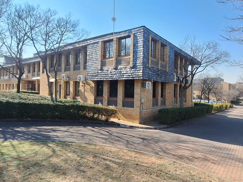 A professional office building featuring a face brick facade, slate roof detailing, and a paved driveway entrance surrounded by established landscaping.