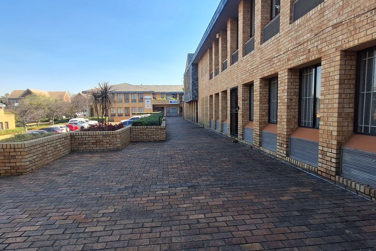 Exterior view of a commercial office building featuring a face brick facade, paved walkway, and secure window treatments.