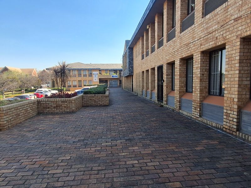 Exterior view of a commercial office building featuring a face brick facade, paved walkway, and secure window treatments.