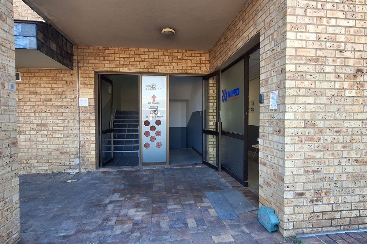Entrance area to an office building featuring face brick exterior, paved flooring, and glass doors leading to an internal staircase.