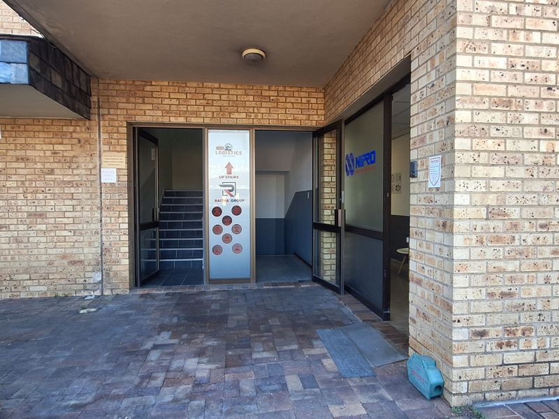 Entrance area to an office building featuring face brick exterior, paved flooring, and glass doors leading to an internal staircase.
