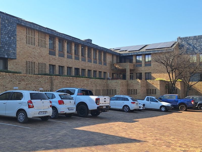 Exterior view of a multi-story office building featuring a face brick facade, slate roof tiles, integrated solar panels, and a paved parking area.