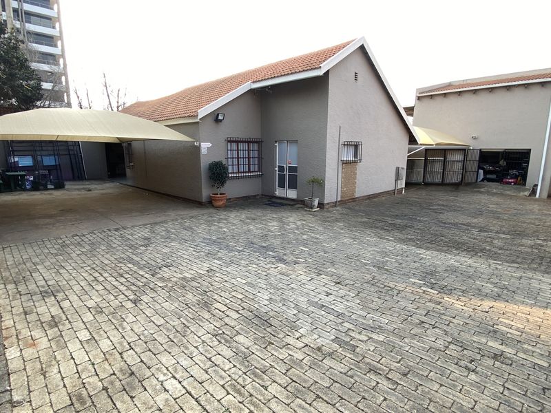 Industrial property exterior featuring a large paved driveway, shade cloth carports, and secure building access with security bars on windows.