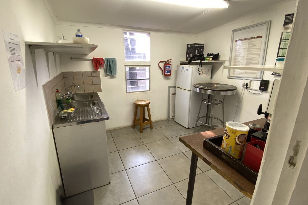 A functional industrial kitchenette featuring a stainless steel sink, tiled splashback, ceramic floor tiles, and wall-mounted shelving for storage.