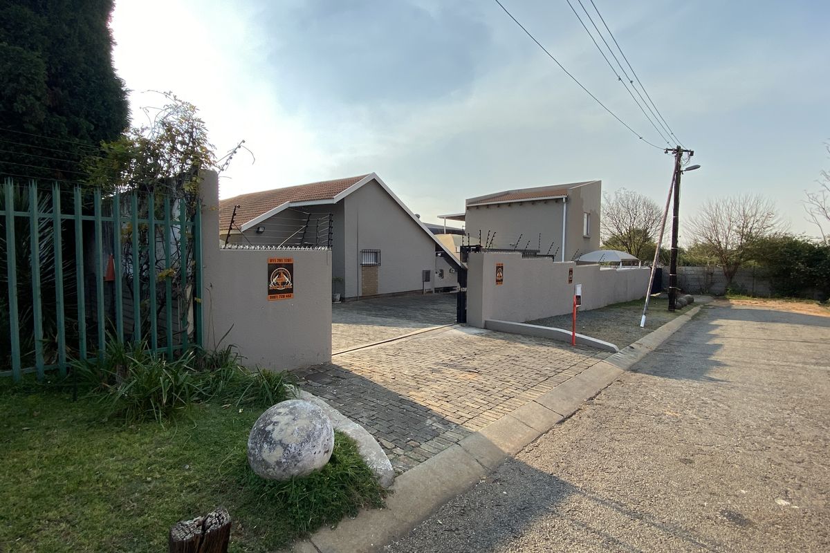 Front exterior view of the industrial property featuring a paved driveway, secure perimeter wall with electric fencing, and gated access.