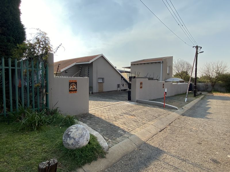 Front exterior view of the industrial property featuring a paved driveway, secure perimeter wall with electric fencing, and gated access.