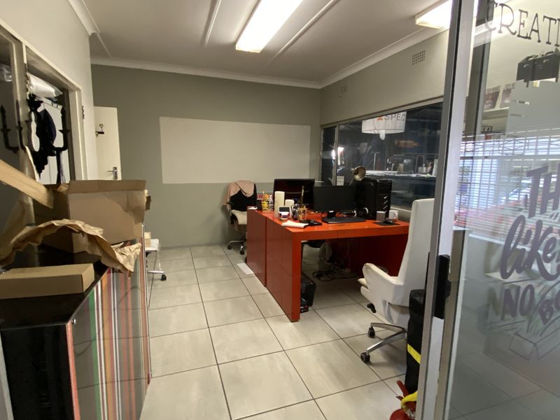 A functional office space featuring tiled flooring, fluorescent lighting, and a glass partition entrance, suitable for a professional work environment.