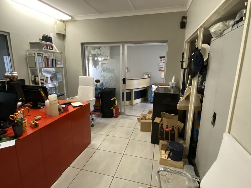 Functional office space featuring tiled flooring, built-in storage cabinetry, and a sliding glass door leading to an adjacent reception or workspace area.