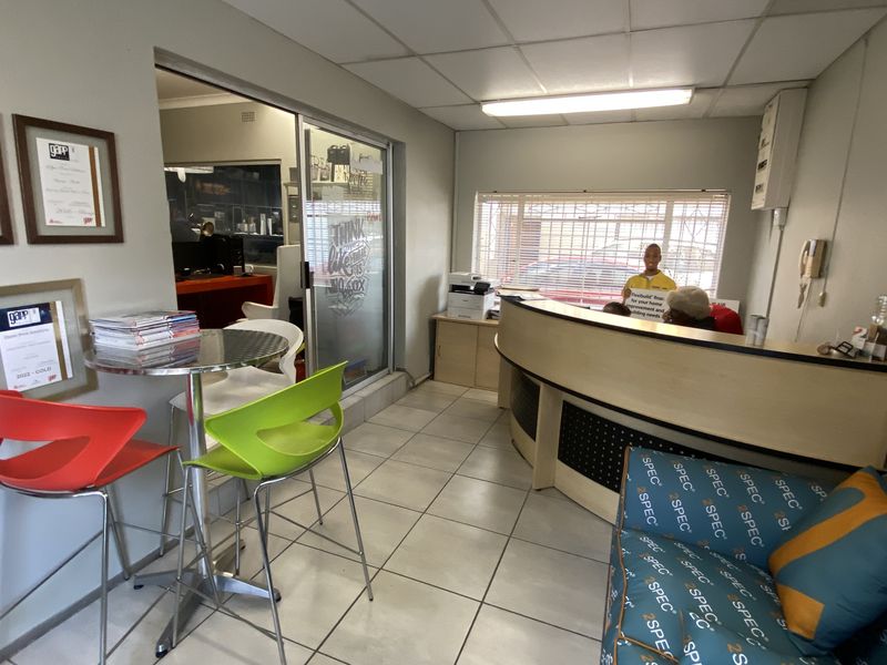 A functional office reception area featuring a curved reception desk, tiled flooring, drop ceiling, and a sliding glass door leading to an adjacent workspace.