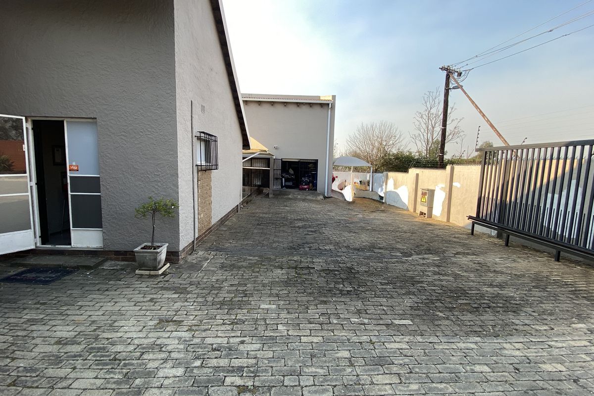 Rear exterior area featuring a paved driveway, secure perimeter walling, and access to the main building structure.